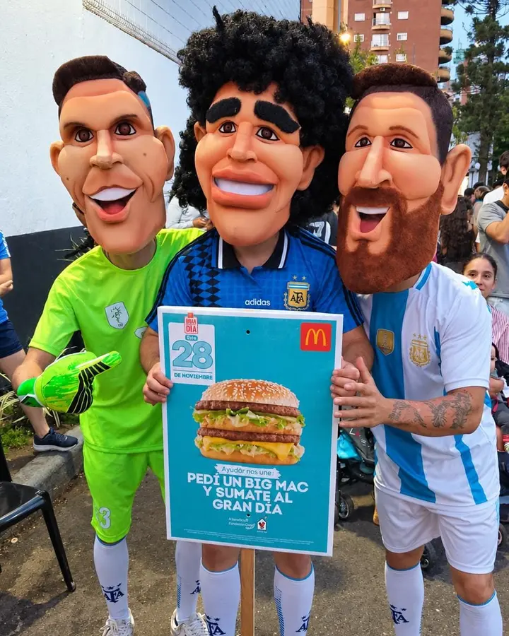 Cabezones de Messi, Maradona y el Dibu con un cartel de McDonald's